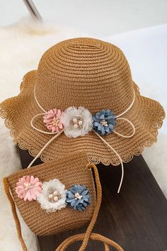 two hats with flowers on them sitting on top of a wooden board next to a bag