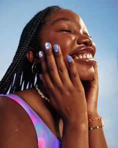 a woman with blue and pink nail polish holding her hands to her face, smiling