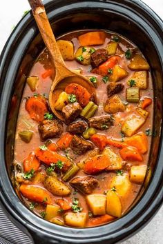 a wooden spoon in a slow cooker filled with beef stew and carrots,