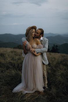 a man and woman embracing each other while standing on top of a grass covered hill