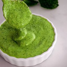 a small white bowl filled with green sauce and broccoli in the back ground