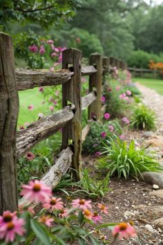 a wooden fence surrounded by flowers next to a dirt path in the grass and trees