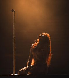 a naked woman sitting on top of a wooden floor next to a pole with a street light in the background