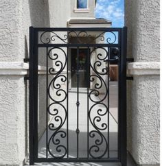 an iron gate in front of a white stucco building with blue sky and clouds behind it