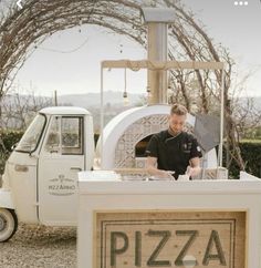 a man is making pizza at an outdoor food stand in front of a white truck