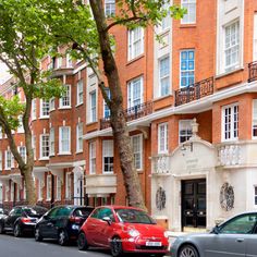 several cars parked on the side of a street in front of tall red brick buildings