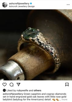 the ring is sitting on top of an old wooden object, and it has a green stone embedded in it