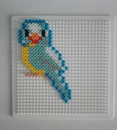 a bird made out of legos sitting on top of a white board with blue and yellow beads