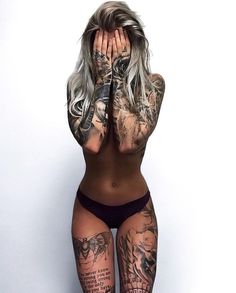 a tattooed woman covers her face with her hands while standing in front of a white wall