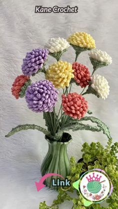 a vase filled with lots of colorful flowers on top of a white table next to a green leafy plant