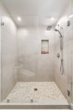 a walk in shower sitting next to a white tiled wall and floor with glass doors