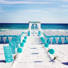 a beach wedding set up with blue and white decorations on the sand near the ocean