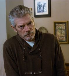 an older man with grey hair wearing a brown sweater