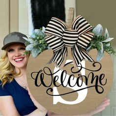 a woman holding up a welcome sign with a bow on it's front door