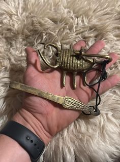 a hand holding a small gold scorpion charm on it's wrist, next to a white rug