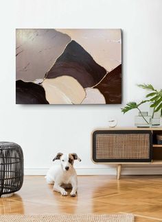 a dog is sitting on the floor in front of a wall with an abstract painting