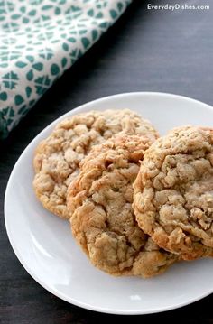 three oatmeal cookies on a white plate next to a green and white napkin