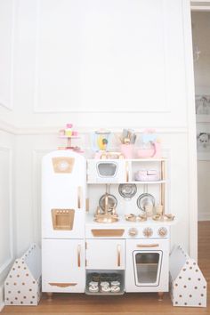 a white toy kitchen with wooden floors and walls