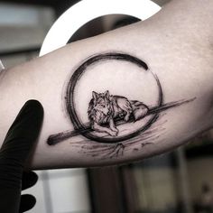 a man's arm with a tattoo of a wolf laying on top of a circle