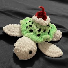 a stuffed turtle with a santa hat on it's head sitting on a black blanket