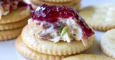 crackers with jelly and cream filling on them sitting on a white surface next to cookies