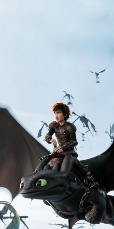 a young boy riding on the back of a black dragon in front of flying birds