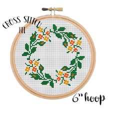 a cross stitch wreath with orange and yellow flowers is shown on a white background in the hoop