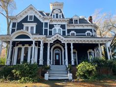 a black and white victorian style house with porches on the second floor is surrounded by greenery