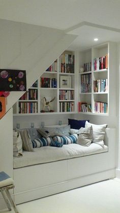 a living room filled with lots of furniture and bookshelves next to a stair case