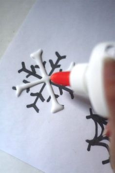 someone is drawing a snowflake with white and black paint on paper that has been drawn onto