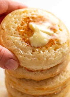 a hand holding a stack of pancakes with butter on top