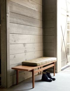 a wooden bench sitting in front of a wall next to a pair of black shoes