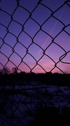 an airplane is flying in the sky behind a chain link fence at sunset or dawn