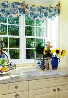 sunflowers and dishes are on the counter in this kitchen window sill with blue and white curtains