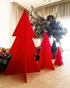 three red christmas trees sitting on top of a carpeted floor next to a window