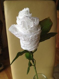 a white rose in a glass vase on a chair with the seat back turned down