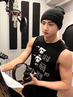 a young man sitting in front of a laptop computer while wearing a beanie and listening to headphones