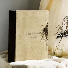 a book sitting on top of a bed next to a vase with flowers in it