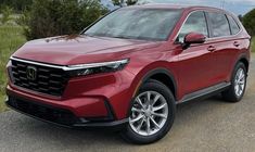 a red honda suv is parked on the side of the road with trees in the background