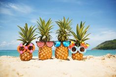 three pineapples wearing sunglasses on the beach