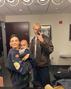 a man holding a baby taking a selfie with his cell phone while standing next to a woman