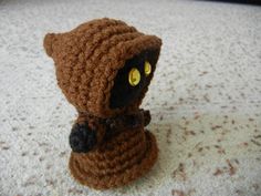 a small crocheted stuffed animal is sitting on the floor with its hood up