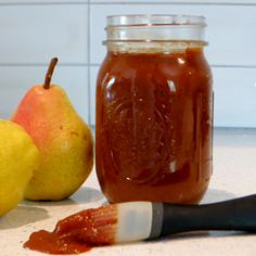 a jar filled with jam next to two pears and a knife on a counter