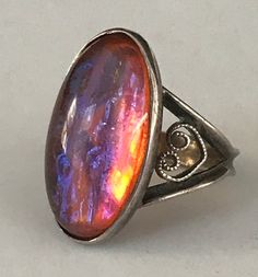 This lovely vintage Sterling Silver ring has an oval shaped bezel set dragon's breath stone that is 3/4" long. The sides have ornate heart shaped scrolls and the back is smooth and comfortable to wear, There is a very slight bend to one side of the band which is barely noticeable. Otherwise, this ring, which is a size 3 1/2, is in very good vintage condition. Please see all photos and feel free to ask any questions.Thank you for looking! Iridescent Oval Spiritual Rings, Spiritual Iridescent Oval Rings, Art Nouveau Style Oval Ring For A Gift, Iridescent Opal Cabochon Ring For Anniversary, Vintage Collectible Opal Ring With Oval Cabochon, Vintage Oval Cabochon Opal Ring Collectible, Vintage Oval Cabochon Opal Ring Gift, Antique Oval Opal Ring As Gift, Antique Oval Opal Collectible Ring