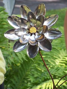 a large metal flower sitting on top of a lush green plant filled with leaves and flowers