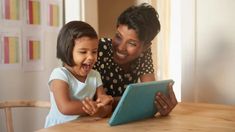 a woman and child looking at an electronic device on the table in front of them