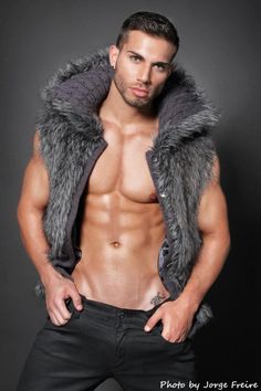 a shirtless man in black jeans and grey fur vest posing for the camera with his hands on his hips