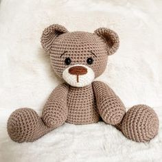 a crocheted teddy bear sitting on top of a white blanket