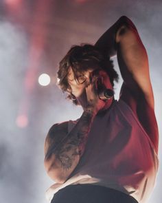 a man with tattoos on his arm holding a cell phone to his ear while standing in front of a microphone