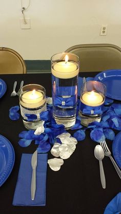 the table is set with blue plates, silverware and candlelight centerpieces